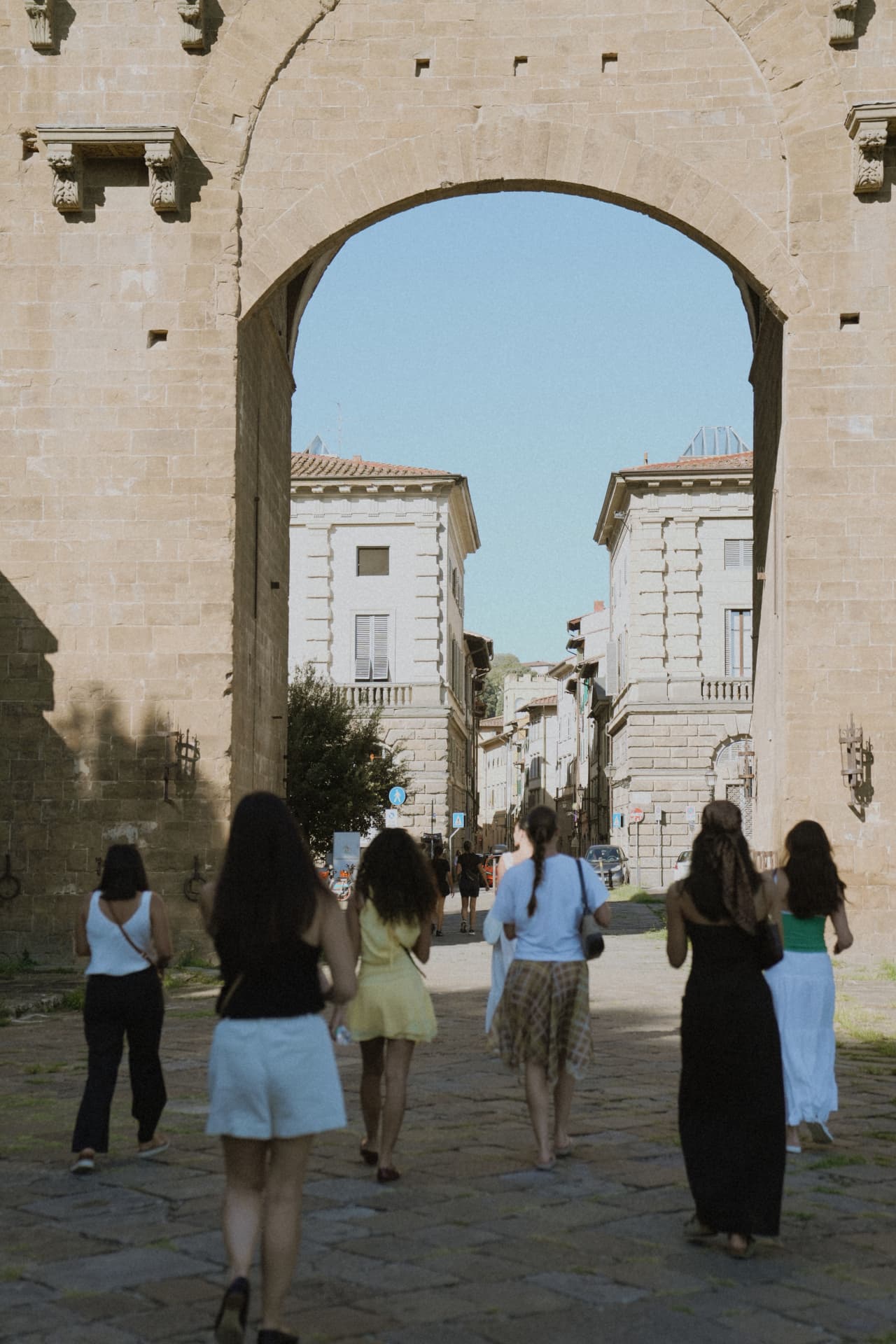 Six women walking away through a stone archway into the streets of Florence