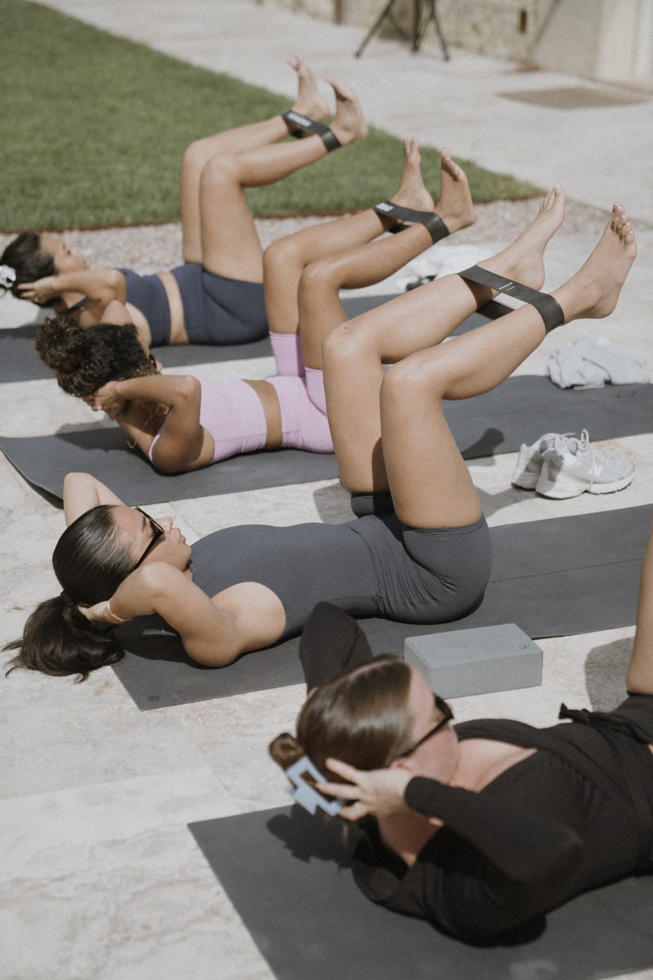 Four women doing mat pilates with resistance bands on a sunlit stone terrace